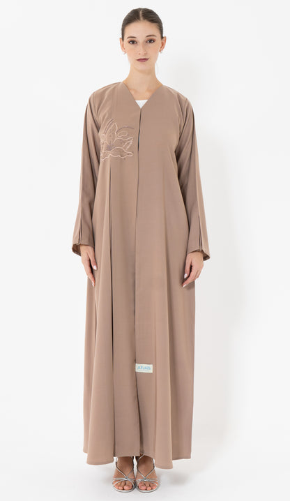 Woman wearing a brown abaya with floral embroidery on a white background