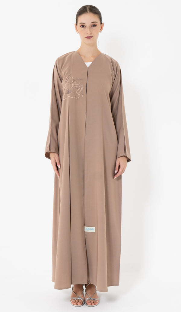 Woman wearing a brown abaya with floral embroidery on a white background