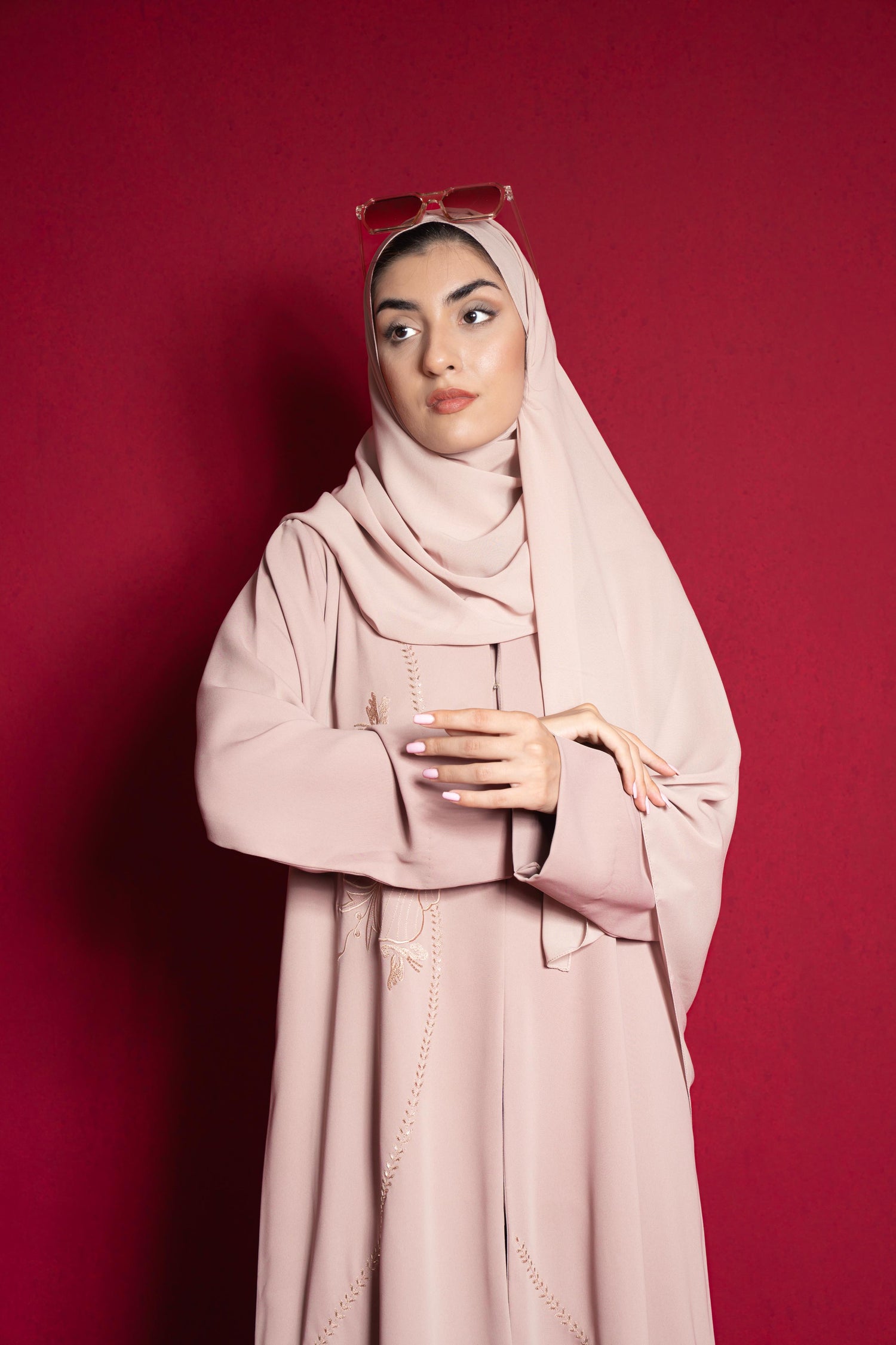 Woman wearing a light pink azael abaya hijab and dress against a red background